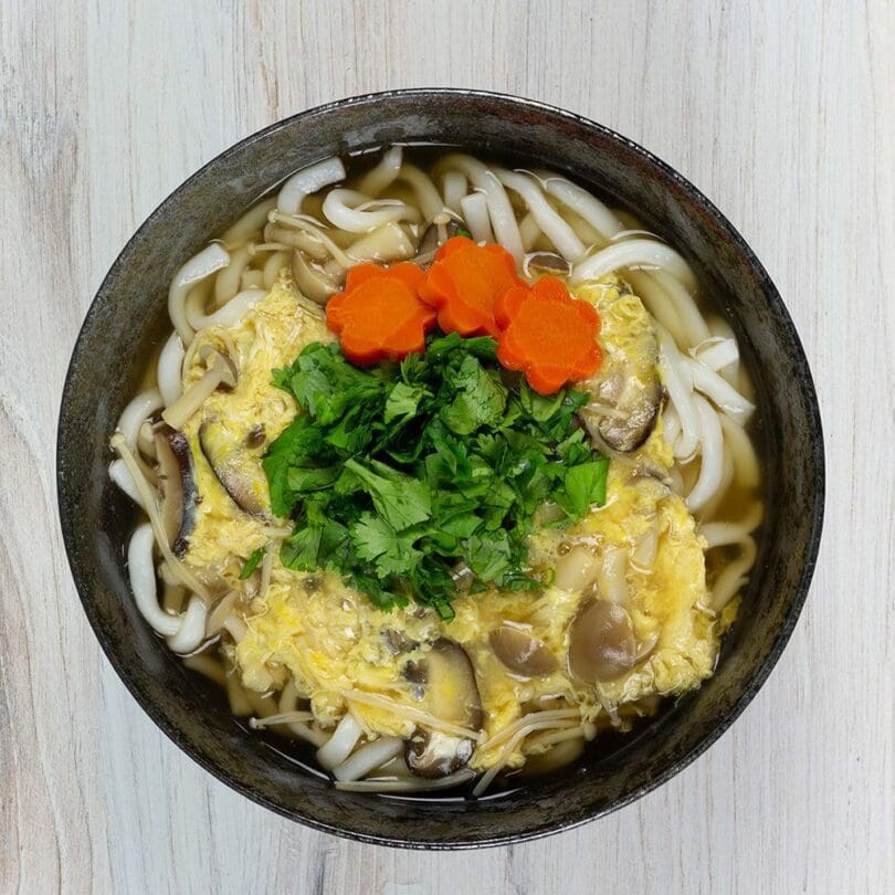 A steaming bowl of udon using Mushroom Flavor Udon topping with 3 kinds of mushroom, egg, and cilantro