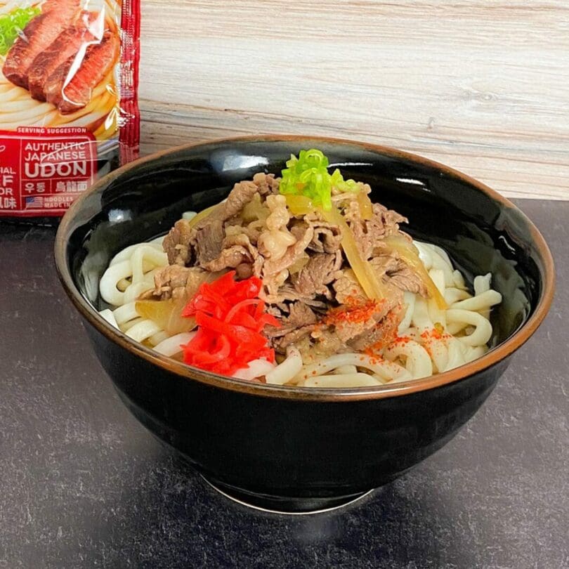 A bowl of hot Beef Flavor Udon topping with beef, onion, scallion, red ginger, and ichimi togarashi (red chili pepper spice)