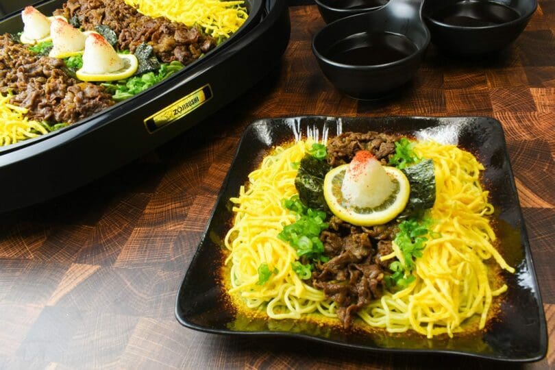 Kawara Yakisoba, a local dish originating from Yamaguchi Prefecture, cooked with Kinshi Tamago (shredded egg crepes), beef, green onions, lemons, seaweed, and grated daikon radish topped with chili peppers