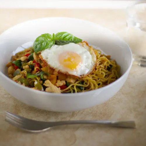 Thai–Style Basil Chicken Yakisoba topping with a sunny side up eggs and basil leaves