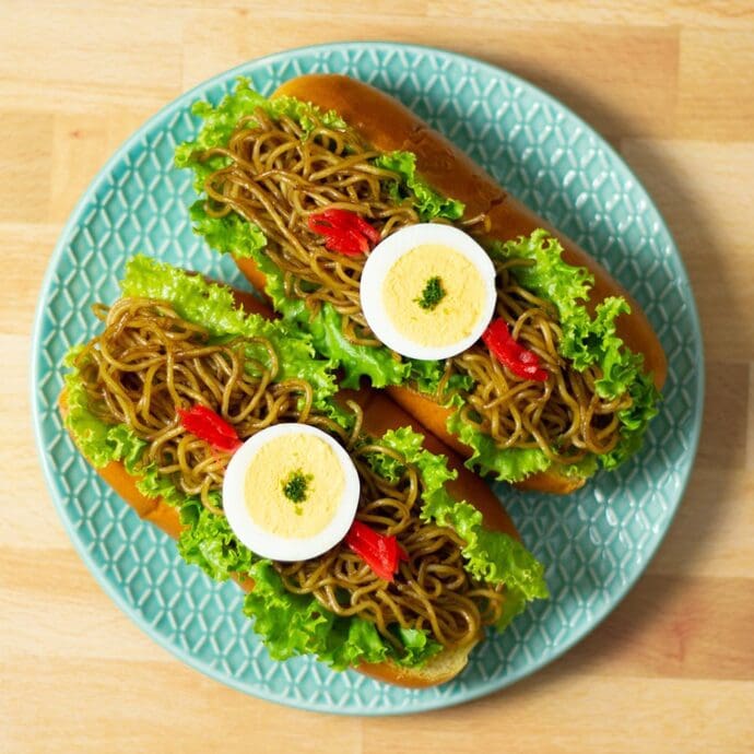 Yakisoba noodles stuffed inside a hotdog bun topping with hardboiled egg, red ginger, and aonori