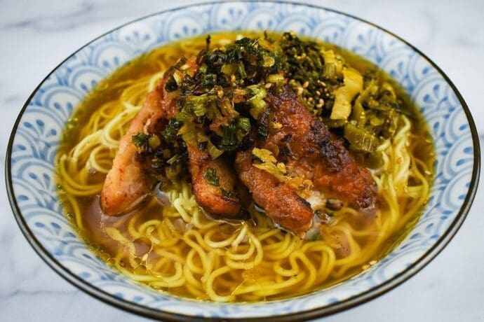 Signature Shio Ramen topping with blackened green onions, marinated chicken thighs with koji salt, and takana (pickled mustard greens)