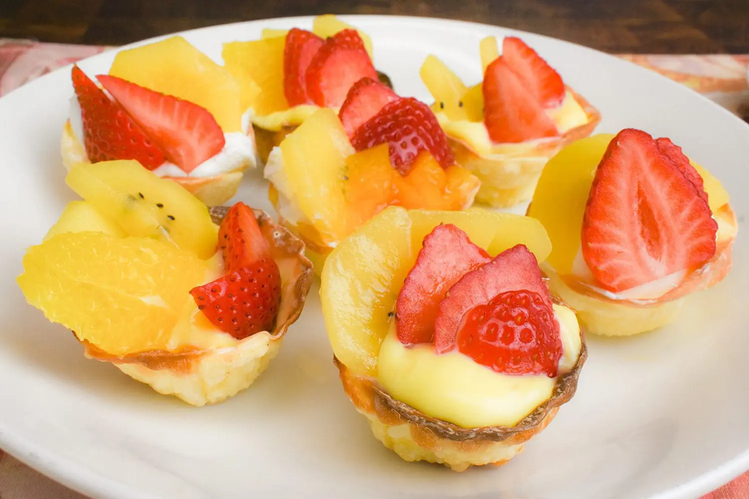 A fruit tart made with gyoza wrapper topped with cream and fruits such as strawberry, kiwi, orange, and peach