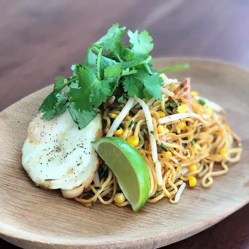 Yakisoba with sauce using a blend of spicy sriracha, soy sauce, and tonkatsu sauce topping with cooked egg, cilantro, lime wedge, and sesame seeds