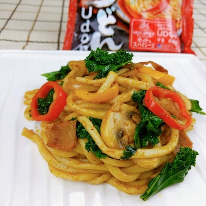 Stir-fried curry udon topping with pork, red bell pepper, yellow bell pepper, kale leaf, onion, and mushrooms