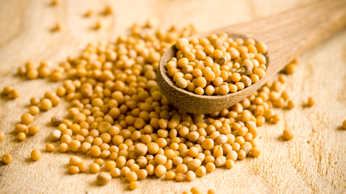 Close-up of yellow mustard seeds spilling from a wooden spoon onto a wooden surface
