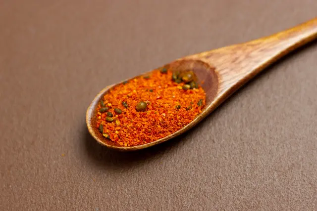 A wooden spoon filled with Japanese shichimi togarashi, a colorful blend of red chili pepper, sesame seeds, and other spices, placed on a brown surface