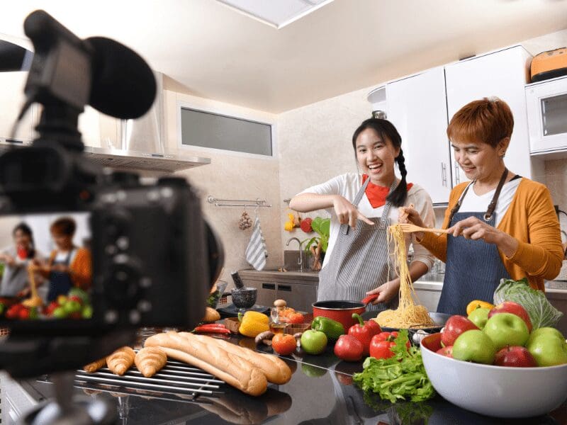 撮影されながらキッチンで一緒に麺料理を作る二人の女性。