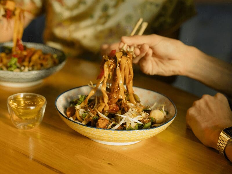 野菜入り炒め麺を箸で食べる人。