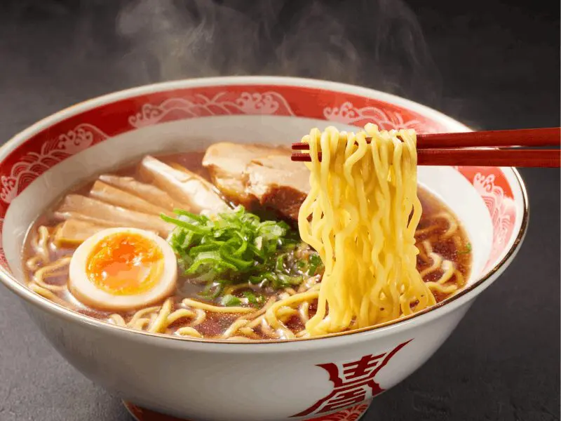 A close-up of steaming ramen noodles lifted with chopsticks
