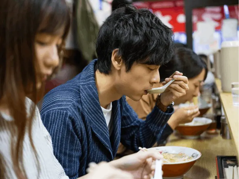 People eating noodle dishes at a counter-style restaurant