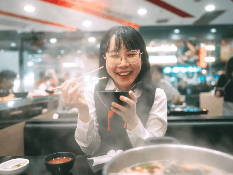 A woman smiling while enjoying a meal at a ramen restaurant