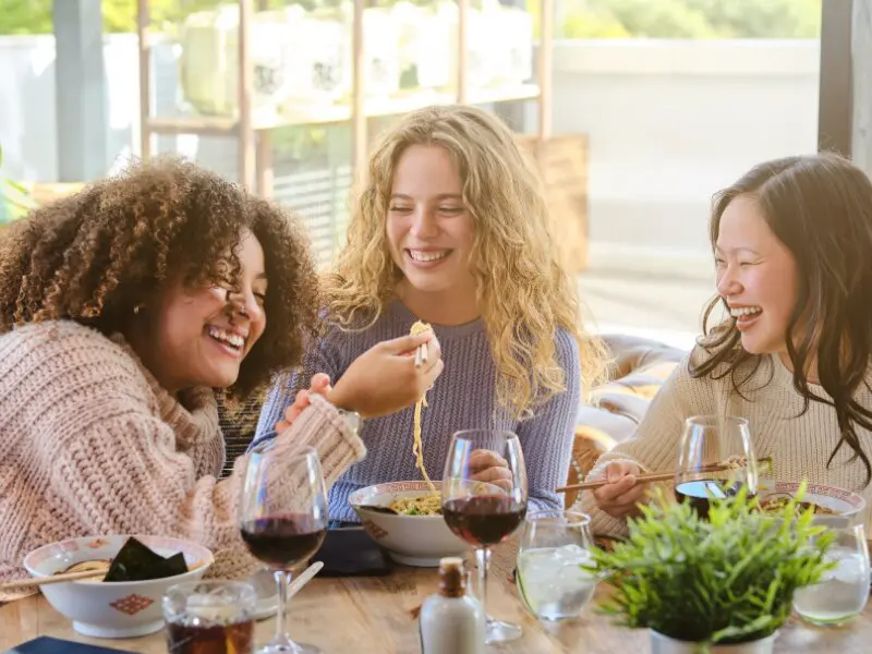 Three women enjoying a meal together with wine at a restaurant table, social dining experience