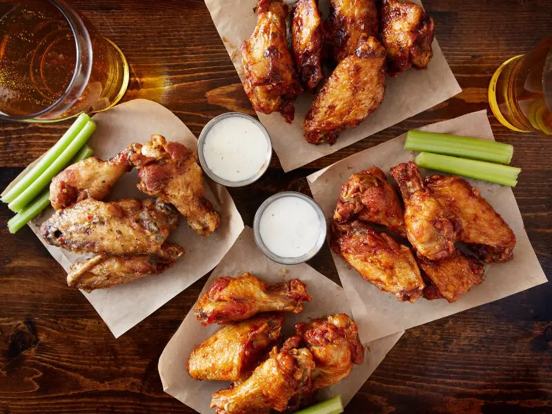 Crispy chicken wings with dipping sauce, celery sticks, and beer on a wooden table, American bar-style food
