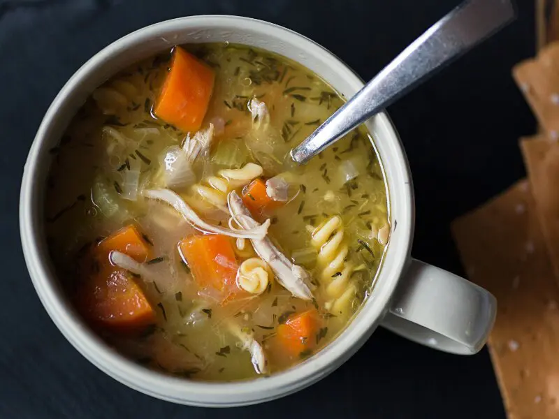 Homemade chicken noodle soup with carrots, celery, and herbs in a white bowl, comforting hot meal