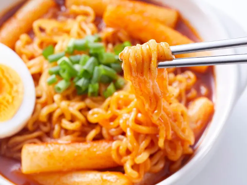 Korean spicy ramen with rice cakes, egg, and green onions in red broth, close-up food shot