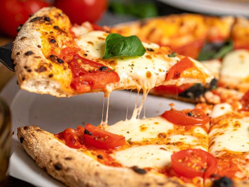 Cheese pizza slice with melted mozzarella and tomato toppings being lifted from a whole pizza