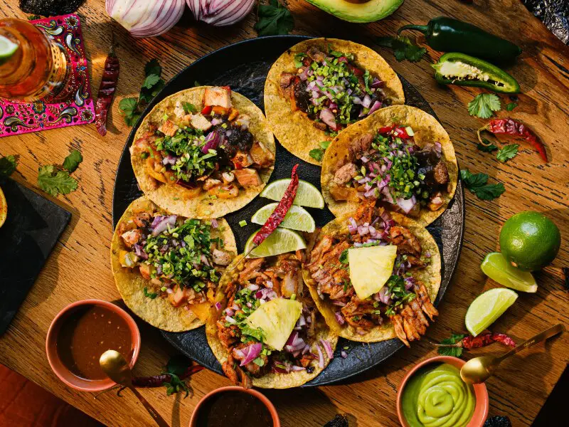 Assorted Mexican tacos with meat, cilantro, onions, and lime on a plate, colorful Tex-Mex food spread